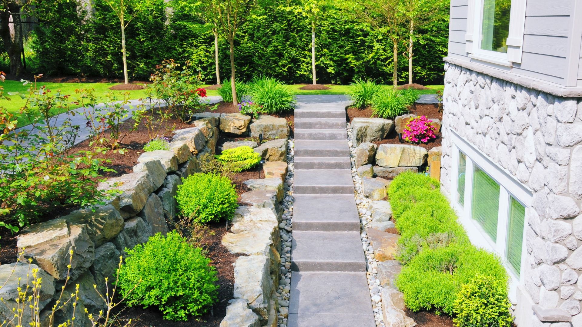 Stone pathway with landscaped garden, green shrubs, and concrete steps