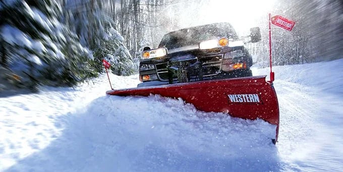 Red snow plow truck clearing snowy road with motion blur in winter forest